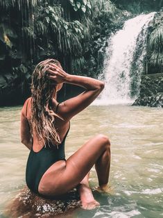 a woman sitting in the water near a waterfall