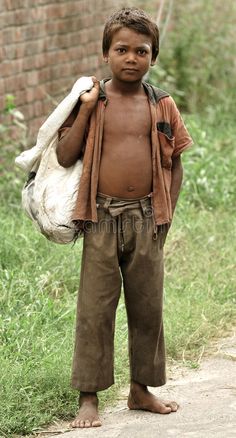 a young boy standing in the grass with a bag on his shoulder and looking at the camera