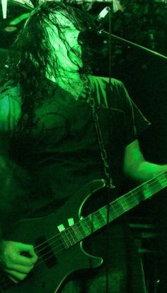 a man with long hair playing a guitar in front of a microphone and green light