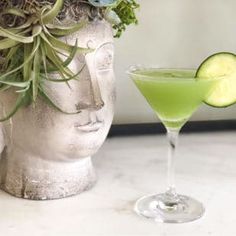 a green drink with cucumber garnish in a glass next to a statue's head