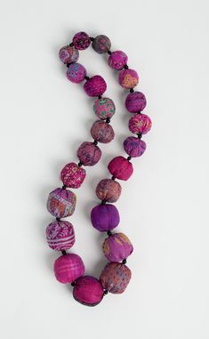 a long necklace with purple and pink beads hanging from it's end on a white surface