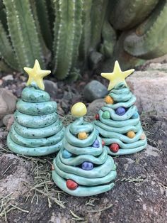 two small ceramic christmas trees sitting on top of a rock next to a cacti