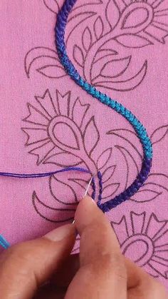 someone is stitching something on a piece of pink fabric with blue thread in the middle