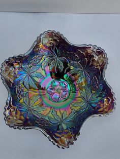 a decorative glass bowl with flowers and leaves on the bottom is shown in multicolored iridescents