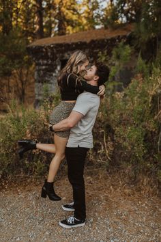 a young man and woman embracing each other in the middle of a dirt road surrounded by trees