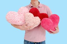 a person holding three knitted hearts in their hands, one is pink and the other is red