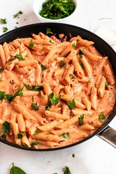 a skillet filled with pasta and sauce on top of a white table next to some parsley