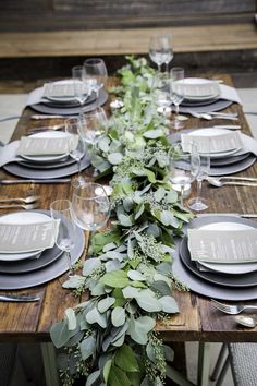 a long table set with place settings and greenery on the top, along with silverware