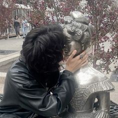 a person sitting on a bench next to a statue with a phone in their hand