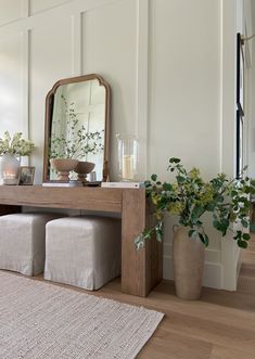 a wooden table topped with a mirror next to a plant and two vases filled with flowers