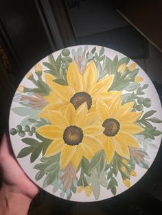 a hand holding a painted plate with yellow flowers on it