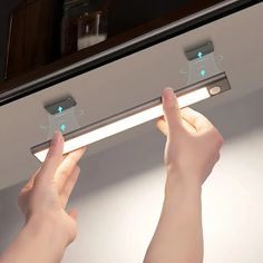 two hands are holding an electronic device in front of a mirror that is lit up