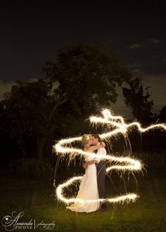 a bride and groom standing in the grass with sparklers coming out of their arms