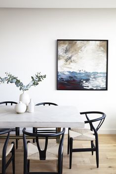 a dining room table with chairs and vases on top of it in front of a painting