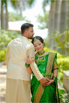 a man and woman standing next to each other in front of some trees with their arms around each other