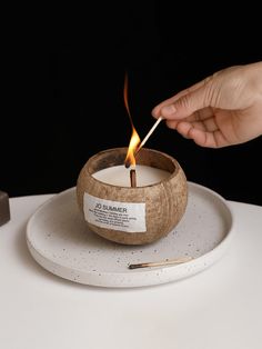 a person lighting a candle on top of a white plate with a stick in it