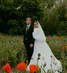 a bride and groom standing in the middle of a field with poppies around them