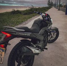 a black motorcycle parked on the side of a road next to grass and trees with an ocean in the background