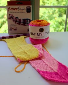 a pink and yellow knitted sock sitting on top of a table next to a box of yarn