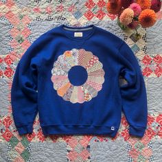 Cozy pre-owned sweatshirt with vintage quilt patch. This patchwork appliqué was repurposed from an unfinished quilt made in my favourite pattern - the Dresden Plate. It consists of 20 'petals' in colourful, vintage floral prints.  Original Label: Russell Athletics Original Label Size: Label removed. Men's size L based on measurements. Chest measured flat, pit to pit: 24 inches Length: 27 inches Colour: Cobalt blue Content: No label. Feels like a cotton/polyester blend. Care: Handwash. Lay flat to dry. Because we are using vintage/pre-owned textiles and clothing, there may be minor discolourations and/or signs of wear. All clothing and accessories are sold as is. Kindly review all photos and contact us if you have any questions. Cotton Patchwork Crew Neck Sweatshirt, Cotton Patchwork Sweatshirt With Crew Neck, Blue Cotton Tops With Floral Patchwork, Retro Cotton Patchwork Sweatshirt, Vintage Cotton Patchwork Sweatshirt, Vintage Crew Neck Patchwork Sweatshirt, Vintage Crew Neck Sweatshirt With Patchwork, Vintage Patchwork Sweatshirt, Quilt Dresden Plate