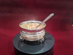 a silver bowl with a spoon in it sitting on a black stand against a red background