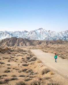 a person walking down a dirt road with mountains in the background