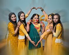 four women in yellow dresses are making a heart shape with their hands while standing next to each other