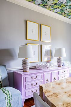 a dining room table with two lamps on top of it next to a purple dresser