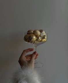 a person holding a wine glass with gold balls in it and some white fur on the side