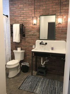 a white toilet sitting next to a bathroom sink under a mirror on a brick wall