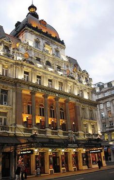 an old building lit up at night with people walking in front and on the sidewalk