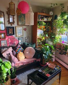 a living room filled with lots of plants and pictures hanging on the wall next to a couch