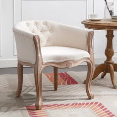 a white chair sitting on top of a rug next to a table with a vase