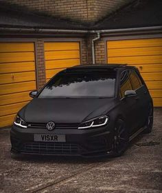 a black vw golf gtr parked in front of two yellow garage doors with the door open