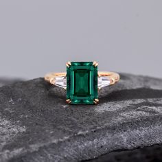 an emerald and diamond ring sitting on top of a rock