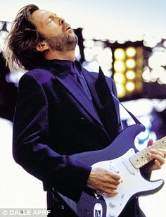 a man in a suit playing an electric guitar with his eyes closed and head tilted to the side