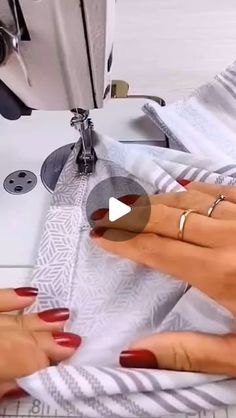 two hands on a sewing machine with red fingernails