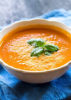 a white bowl filled with carrot soup on top of a blue towel and a green leafy garnish