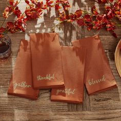 four orange towels with embroidered words on them sitting on a wooden table next to red flowers