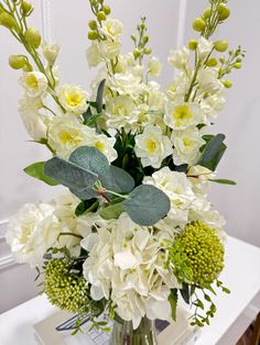 a vase filled with white flowers and greenery