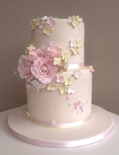 a three tiered white cake with pink flowers on the top and bottom, sitting on a table