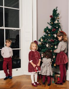 three children standing in front of a christmas tree