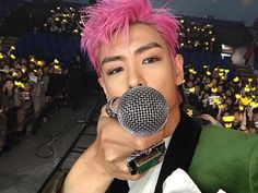 a man with pink hair holding a microphone to his mouth in front of an audience