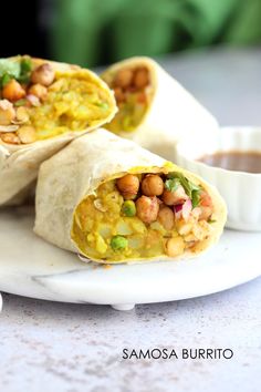 two burritos with chickpeas and vegetables are on a plate next to dipping sauce