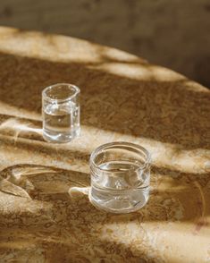 two glass cups sitting on top of a table next to each other with water in them