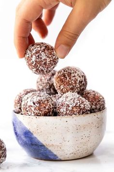 a hand is picking up some chocolate balls from a blue and white bowl on a marble surface