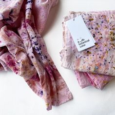 a pile of pink and purple cloths sitting on top of a white table next to a tag