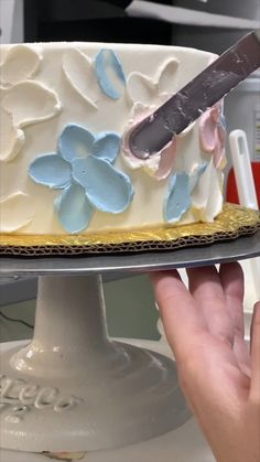 a person holding a knife over a cake on a plate with frosting and flowers