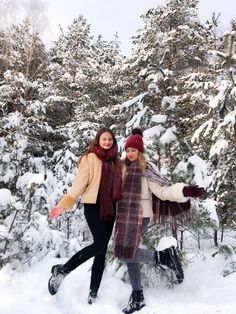 two women standing in the snow with their arms around each other and trees behind them