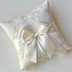 a white lace pillow with a bow on the side and ribbon around the edge, sitting on a white surface